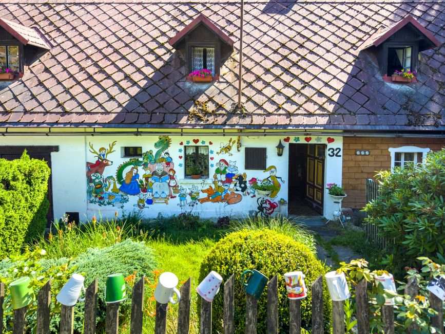 A small painted cottage with a front yard and flower beds.